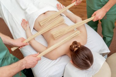 Dört elle masaj yaparken genç bir kadının sırtındaki bambu süpürgeleri..