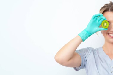 Gülümseyen genç güzellik uzmanı gözlerini yarım parça kivi ile kaplıyor..