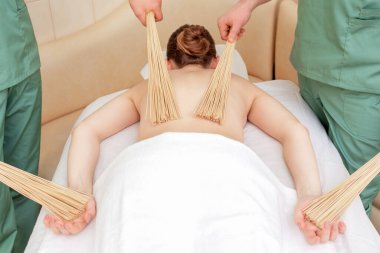 Genç bir kadın dört elle masaj yaptırıyor. Spa salonunda bambu süpürgelerle..