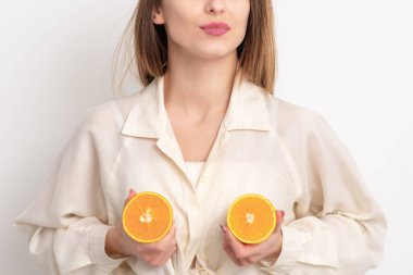 Genç kadın beyaz arka planda iki portakal tutuyor..
