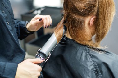 Kuaför kadın saçlarını maşayla kıvırıyor Güzellik salonunda.
