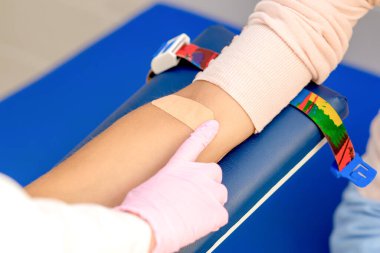 Kauçuk koruyucu eldivenli doktor kan örneği aldıktan sonra koluna yapıştırıcı yapıştırıyor..