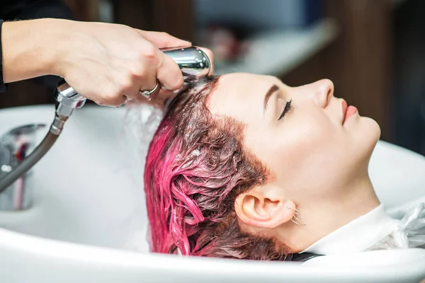 Hairdresser washes pink dyed hair of woman in sink, close up.