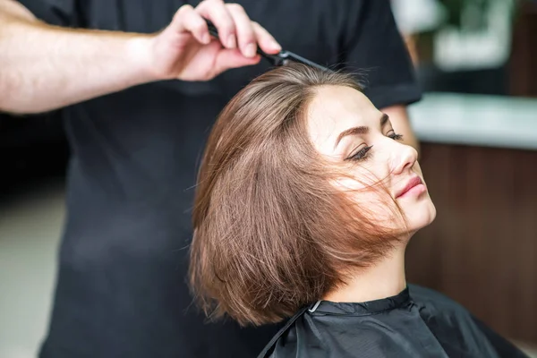 Hairdresser combs hair of woman at hair salon.