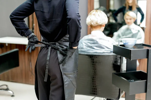 Female hairdresser ties up apron in preparation for a haircut. Toned.
