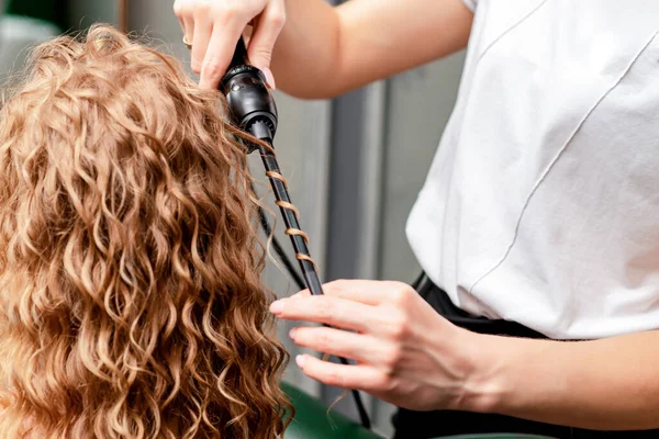 Process of making curls by curling iron in hairdressing salon.
