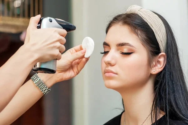 Makeup artist\'s hand sprays with help airbrush on woman\'s face fixing makeup.
