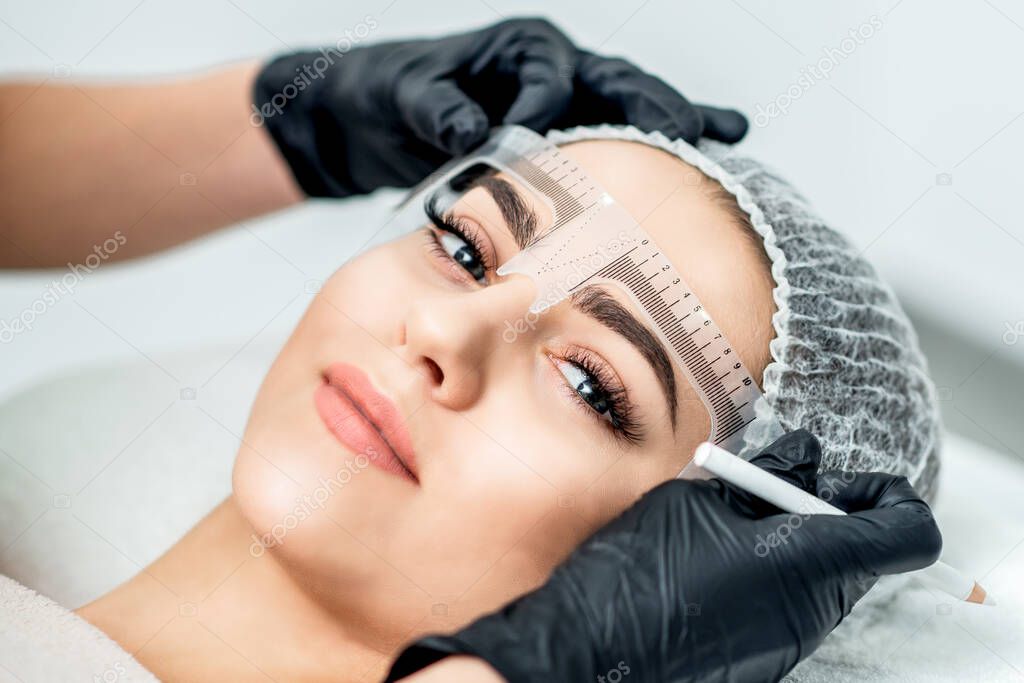 Markup with ruler on eyebrows of yong woman during permanent make up.