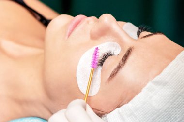 Güzellik salonunda kirpik uzatma işlemi sırasında kirpik fırçası kullanan bir kozmetikçi..