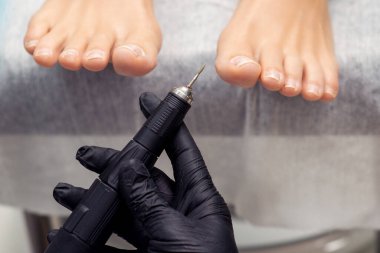 Pedikürcünün eli ayak parmaklarının arka planında pedikür için elektrik makinesini tutuyor..