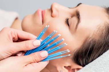 Kozmetik uzmanının ellerinde kirpik pamuğu var. Arka planda genç bir kadının yüzü var. Yakın plan..