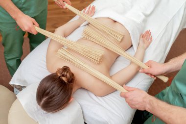 Genç bir kadın dört elle masaj yaptırıyor. Spa salonunda bambu süpürgelerle..