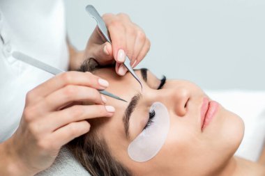 Kirpik için cımbız tutan güzellik uzmanı genç bir kadının yüzüne yakın, kapat..
