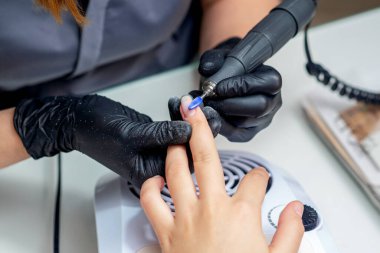 Manikür ustası, güzellik salonundaki ojeleri özel elektrikli makineyle temizliyor..