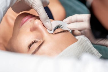 Bir güzellik salonunda kirpiklerini uzatan genç bir kadın, yakın çekim, kirpik uzatma prosedürü.