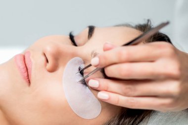 Kozmetik uzmanı, takma kirpiklerini kadının gözüne cımbızla yapıştırırken kirpik uzatma prosedürü uyguluyor..