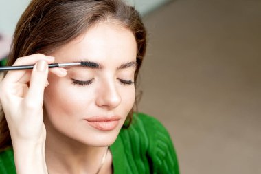 Kaş fırçası ile kaş makyajı yaptıran genç bir kadın..
