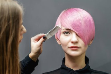 Kuaför, gri arka planda kısa pembe saç modelini tarıyor..