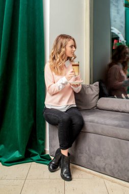 Kanepede kahve içen genç ve güzel bir kadın pencereden içeri bakıyor..