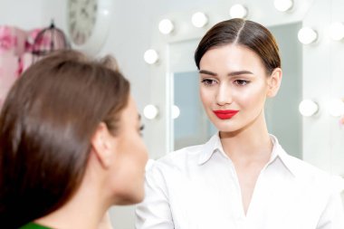 Makyöz, genç bir kadın için profesyonel makyaj yapıyor. Makyöz, müşteriyle çalışmaya hazır..