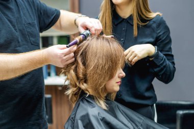 Güzellik salonunda saç maşasıyla saç kıvıran profesyonel kuaförü kapat..