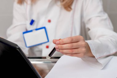 Hemşire kan testi tüpünü tablet cihazına kan örneği yazarken tutuyor..