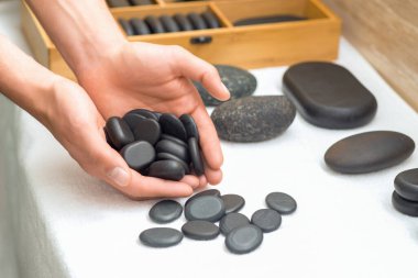 Yumuşak cilalı sıcak masaj kaplıcasında adamın elindeki siyah taşlar rahatlatıcı spa salonundaki masada.