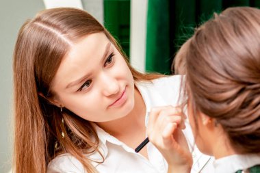 Güzellik salonunda profesyonel makyöz tarafından makyaj yaptıran genç bir kadın..