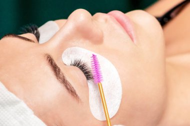 Kozmetik uzmanı, güzellik salonunda kirpik uzatma işlemi sırasında kirpik fırçası kullanır..