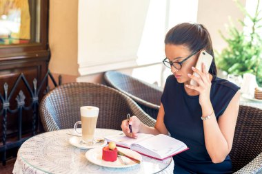 Bir kafede çalışan gözlüklü bir iş kadını telefonda konuşuyor. İş konsepti