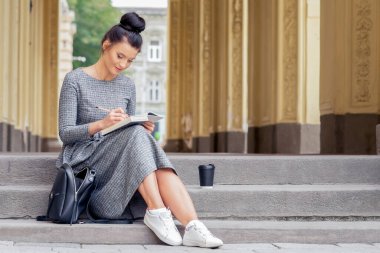 Genç üniversite öğrencisi kadın üniversitenin merdivenlerinde kitap okuyor. Öğrenci kız, üniversite binasının merdivenlerinde kitap okuyor..