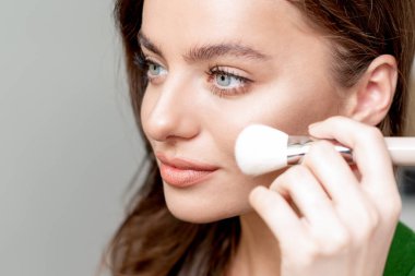 Makyaj fırçası kullanan bir kadının portresini yakından çek. Yüzüne kuru makyaj malzemesi dök. Makyaj malzemesi..