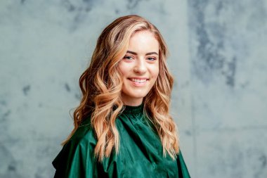 Gri arkaplanda mükemmel kıvırcık saç stili ve makyajı olan güzel, gülümseyen beyaz, sarışın bir kadının portresi..