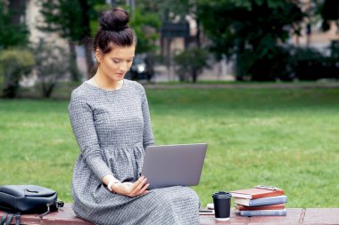 Beyaz bir kız öğrenci parktaki bankta dizüstü bilgisayar kullanıyor. Öğrenci kız parkta bir bankta otururken dizüstü bilgisayar kullanır ve ders çalışır..