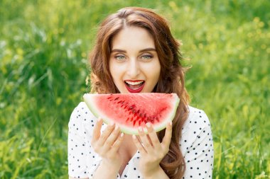 Güzel genç bir kadın yeşil çimlerin üzerinde olgun kırmızı karpuz dilimlerini ısırıyor..