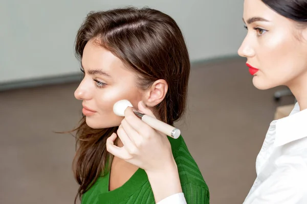 Makeup artist using makeup brush applying dry cosmetic tonal foundation on woman's face.