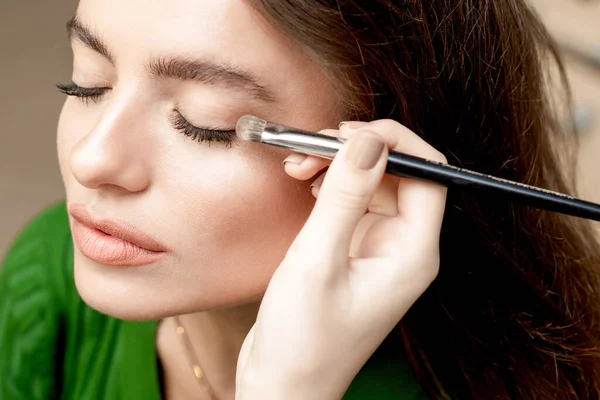 Maquiagem Artista Aplica Sombra Com Escova Para Mulher Jovem — Fotografia de Stock