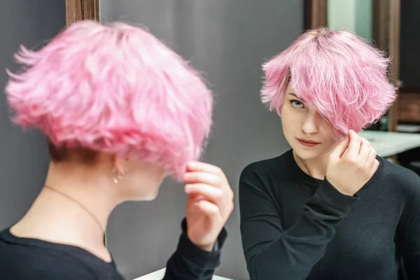 Pink hair woman with a short hair is looking at the mirror. Beauty concept.