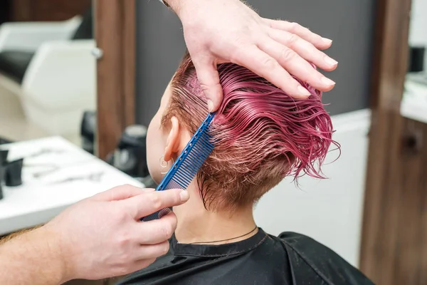 Hairdresser combing hair of woman while cutting. Hands of hairstylist are combing hair of woman close up.