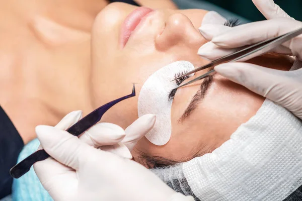 Procedure of eyelashes extension on woman eye with long eyelashes during eyelash extension in salon.