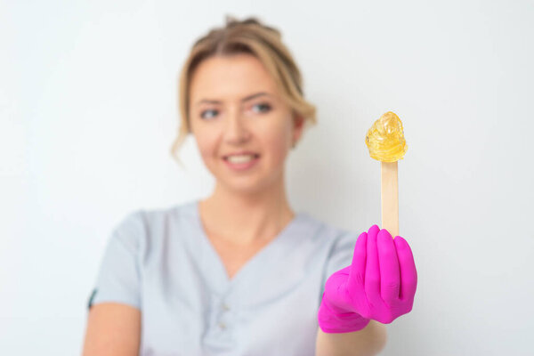 Beautician shows stick with wax for epilation on white background.