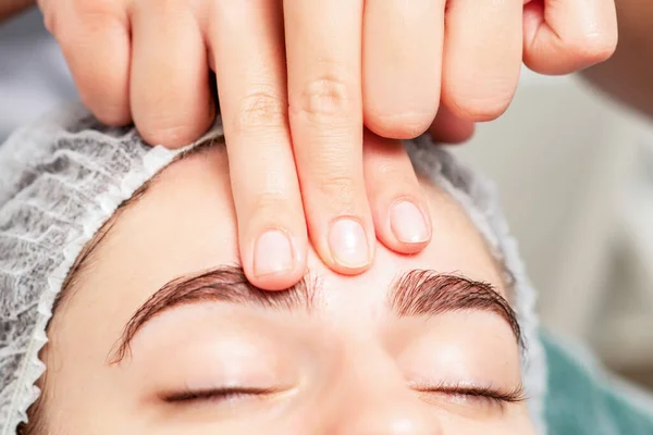 Massage of forehead of woman by fingers of massage therapist at beauty salon close up.
