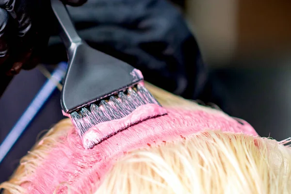 ブラシは 女性のクローズアップの白い髪にピンクの染料を適用します 美容室でのヘアカラー — ストック写真