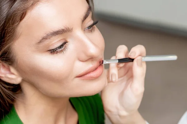 Makeup artist applies lipstick on woman lips, make up in process.