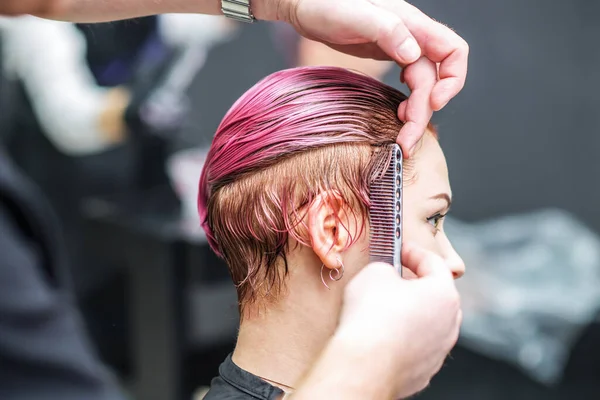 Hairdresser combs hair of woman at hair salon.