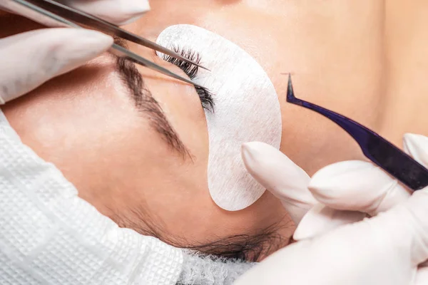 Procedure of eyelashes extension on woman eye with long eyelashes during eyelash extension in salon.