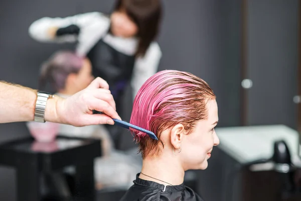 Hairdresser combs hair of woman at hair salon.