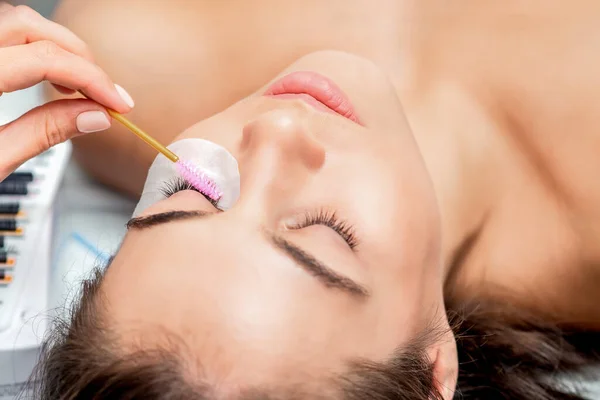 Stylist holding brush and making lengthening lashes for woman, close up.