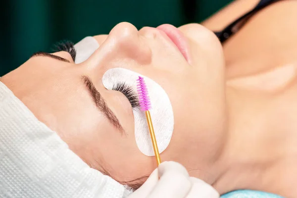 Cosmetologist uses eyelash brush for eyelashes during eyelash extension procedure in a beauty salon.