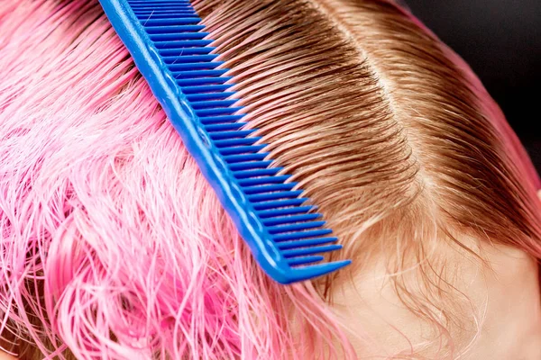 Hands hairdresser combs pink hair of young woman close up in hair salon.